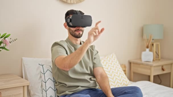 Молодой латиноамериканец в очках виртуальной реальности играет в видеоигру в спальне - Кадры, видео