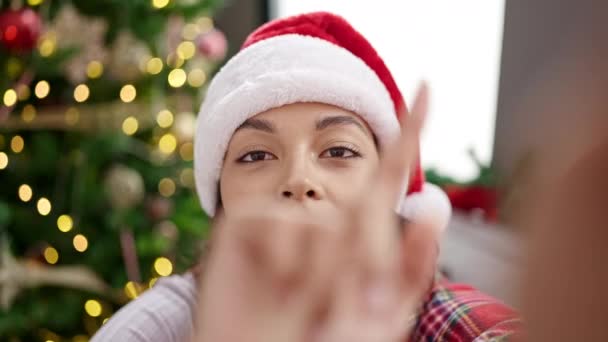 Joven mujer hispana hermosa haciendo una videollamada sentada en el sofá por el árbol de Navidad en casa - Imágenes, Vídeo