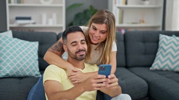 Hombre y mujer pareja usando teléfono inteligente sentado en el sofá en casa - Metraje, vídeo