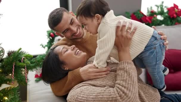 Ζευγάρι και γιος αγκαλιάζονται καθισμένοι στον καναπέ δίπλα στο χριστουγεννιάτικο δέντρο στο σπίτι - Πλάνα, βίντεο