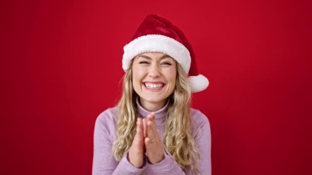 Young blonde woman wearing christmas hat clapping hands applause over isolated red background - Footage, Video
