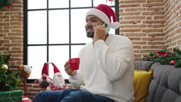 Uomo afroamericano che parla su smartphone bevendo caffè festeggiando il Natale a casa - Filmati, video