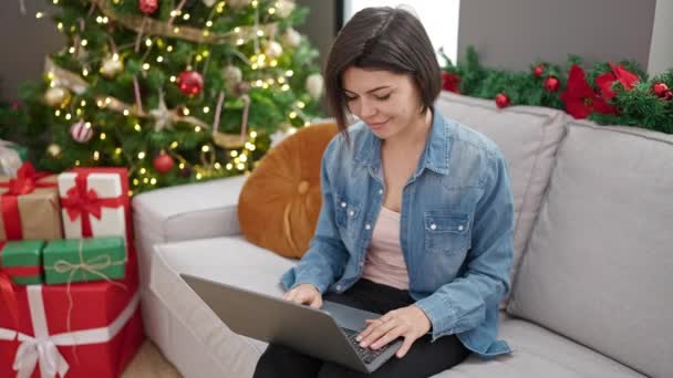 Νεαρή καυκάσια γυναίκα που χρησιμοποιεί φορητό υπολογιστή κάθεται στον καναπέ στο σπίτι - Πλάνα, βίντεο