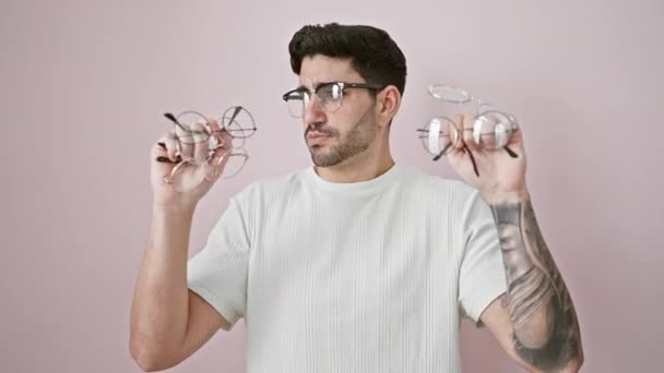 Mladý hispánec muž usměvavý sebevědomě drží brýle přes izolované růžové pozadí - Záběry, video