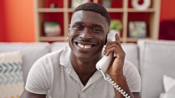 Αφροαμερικάνος μιλάει στο τηλέφωνο κάθεται στον καναπέ χαμογελώντας στο σπίτι - Πλάνα, βίντεο