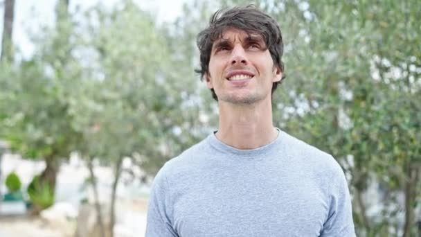 Fiatal spanyol férfi mosolyog magabiztos áll a parkban - Felvétel, videó