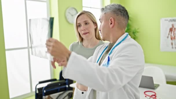 Άντρας και γυναίκα γιατρός και ασθενής έχουν ιατρική γνωμάτευση κοιτάζοντας ακτινογραφία στην κλινική - Πλάνα, βίντεο