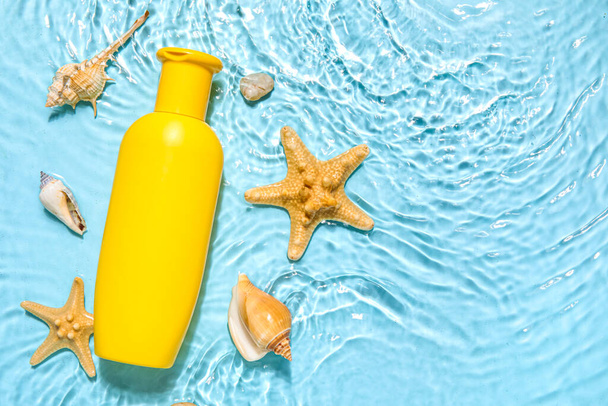 Crème solaire avec étoiles de mer et coquillages dans l'eau sur fond de couleur - Photo, image
