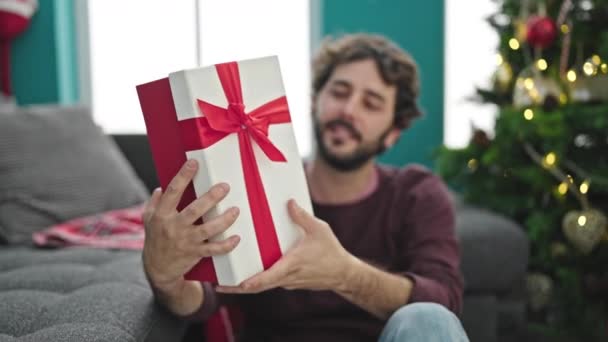 jonge latino man glimlachen zelfverzekerd vasthouden kerstcadeau thuis - Video