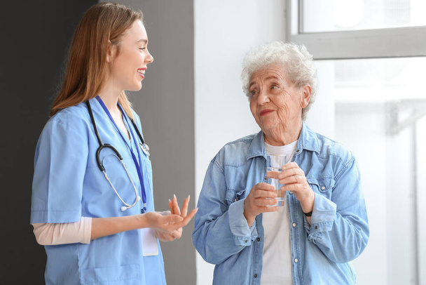 Senior woman with glass of water and female caregiver in room - Photo, Image