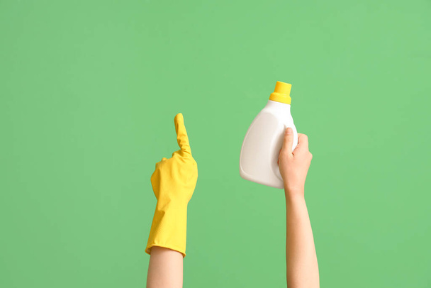 Elinde deterjan şişesi olan bir kadın yeşil arka plandaki bir şeyi işaret ediyor. - Fotoğraf, Görsel