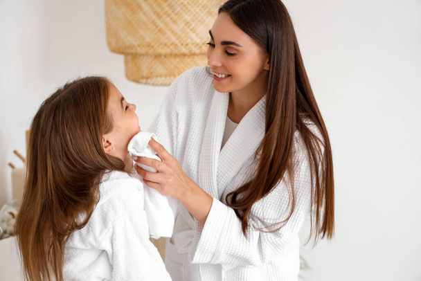 Glückliche Mutter wischt ihrer kleinen Tochter im Badezimmer das Gesicht ab - Foto, Bild