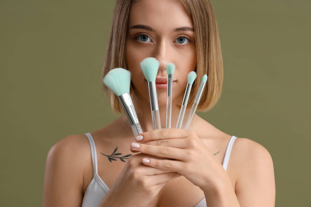 jonge vrouw met set van make-up borstels op groene achtergrond - Foto, afbeelding
