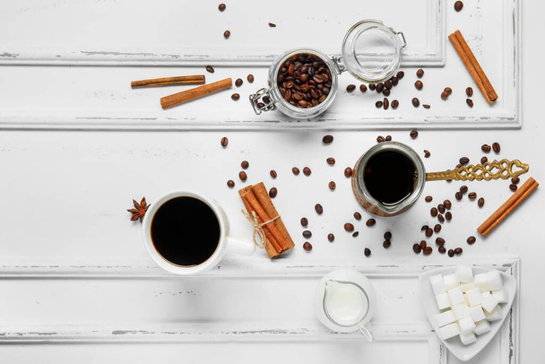 Taza de sabroso café con canela, leche, azúcar, cezve y frijoles sobre fondo de madera blanca - Foto, imagen