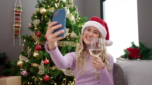 Młoda blondynka świętuje Boże Narodzenie biorąc selfie smartfon pijąc wino w domu - Materiał filmowy, wideo