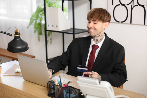 Fiatal üzletember hitelkártyával laptoppal az asztalnál az irodában - Fotó, kép