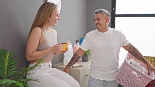 Mies ja nainen pari tilalla kori vaatteita juo kahvia pesutupa - Materiaali, video