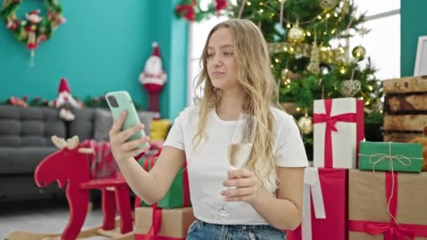 Νεαρή ξανθιά γυναίκα γιορτάζει τα Χριστούγεννα κάνει selfie από smartphone πίνοντας σαμπάνια στο σπίτι - Πλάνα, βίντεο