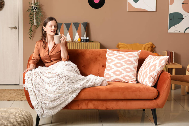 Молода жінка з чашкою чаю і плед відпочиває вдома в осінній день - Фото, зображення