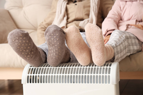 Young couple warming legs on radiator at home, closeup - Photo, Image