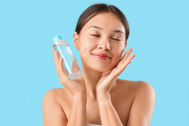 Jovem mulher asiática com garrafa de água micelar no fundo azul, close-up - Foto, Imagem