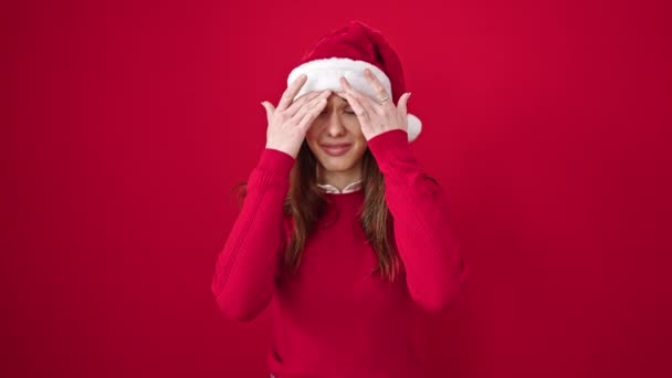 Νεαρή Ισπανίδα που φοράει χριστουγεννιάτικο καπέλο και έχει πονοκέφαλο σε απομονωμένο κόκκινο φόντο - Πλάνα, βίντεο