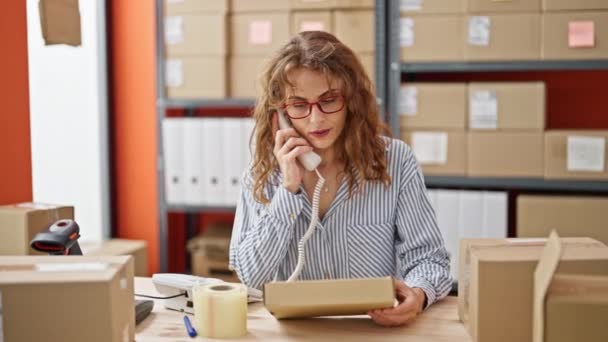 Jovem mulher comércio eletrônico empresário ler informações pacote falando no telefone no escritório - Filmagem, Vídeo