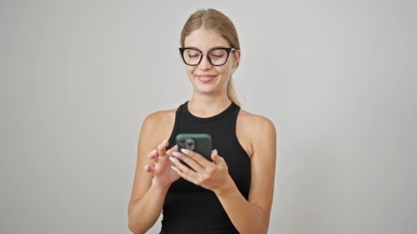 Молода блондинка використовує смартфон, посміхаючись над ізольованим білим тлом - Кадри, відео