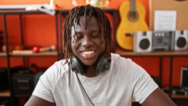 Afrikkalainen amerikkalainen mies muusikko yllään kuulokkeet hymyillen luottavainen musiikin studio - Materiaali, video
