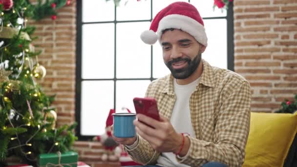 Νεαρός Ισπανός που χρησιμοποιεί smartphone πίνοντας καφέ γιορτάζοντας τα Χριστούγεννα στο σπίτι - Πλάνα, βίντεο