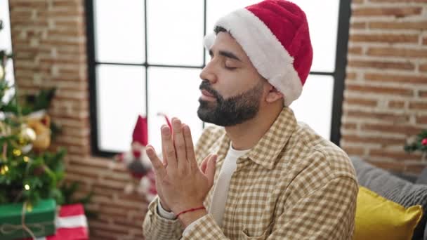 Junger hispanischer Mann feiert Weihnachten und betet zu Hause - Filmmaterial, Video