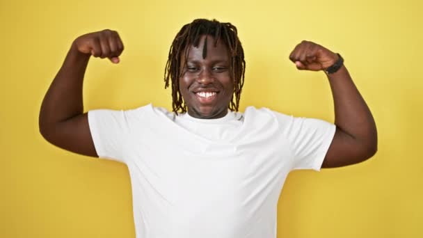 Afrykański Amerykanin uśmiecha się pewnie wykonując silny gest z ramionami na odizolowanym żółtym tle - Materiał filmowy, wideo