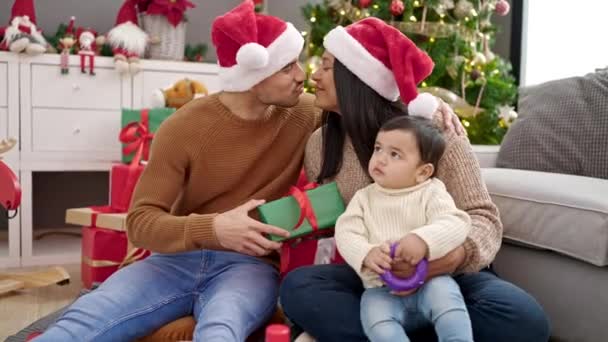 Пара и сын держат подарок сидя на полу у рождественской елки дома - Кадры, видео