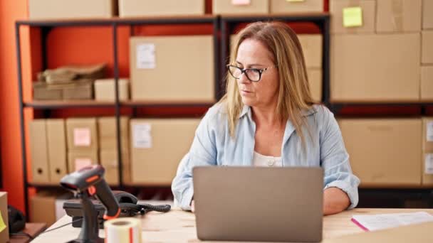 Latynoska kobieta w średnim wieku e-commerce pracownik za pomocą laptopa rozmowy telefonicznej w biurze - Materiał filmowy, wideo