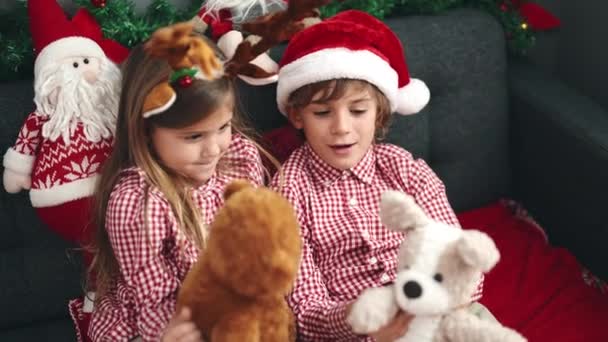 Bratr a sestra hrát s medvídky sedí na pohovce u vánoční dekorace doma - Záběry, video