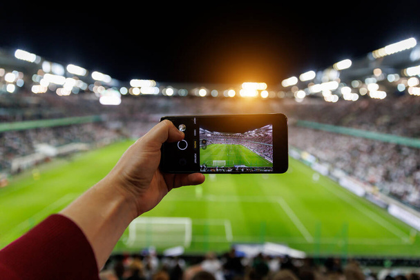 Fan strony ze smartfonem fotografowania meczu piłki nożnej. Korzystanie z kamery komórkowej na stadionie - Zdjęcie, obraz