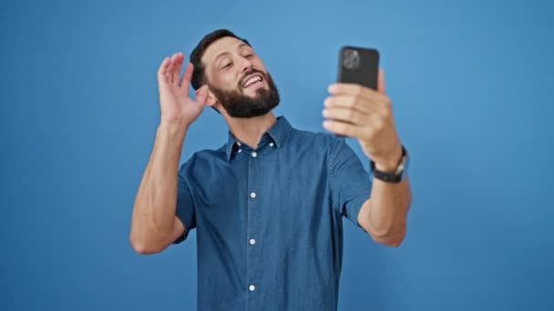 jonge latino man glimlachen zelfverzekerd met video bellen over geïsoleerde blauwe achtergrond - Video