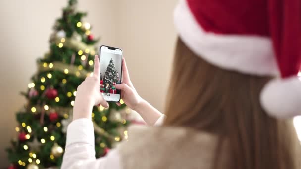 jong blond vrouw maken foto naar kerstboom door smartphone thuis - Video