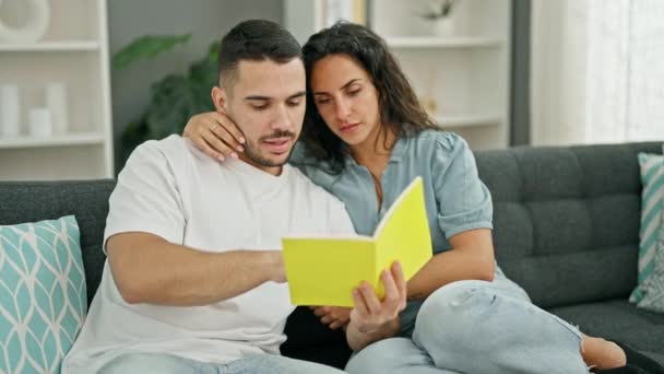 Мужчина и женщина читают книгу сидя дома на диване - Кадры, видео