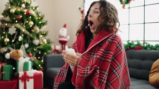 Hispanische Frau mittleren Alters mit Decke bedeckt sitzt zu Hause auf Sofa am Weihnachtsbaum - Filmmaterial, Video