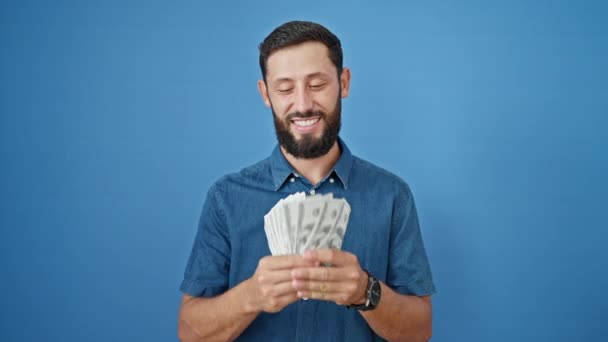 Молодий іспаномовний чоловік посміхається впевнено кидає долари, танцюючи над ізольованим синім тлом - Кадри, відео