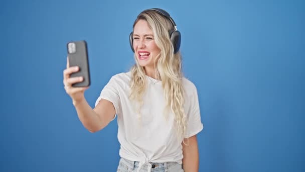 Mladá blondýnka žena usmívá sebevědomě s videohovor přes izolované modré pozadí - Záběry, video