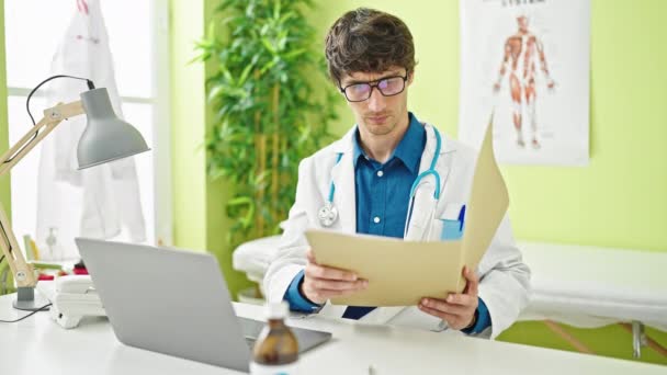 Νεαρός Ισπανός γιατρός διαβάζει ιατρική έκθεση με σοβαρό πρόσωπο στην κλινική. - Πλάνα, βίντεο