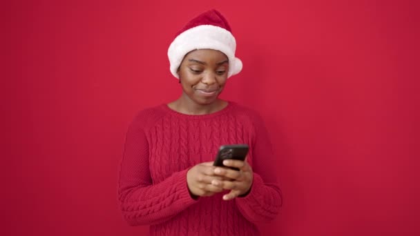 Afrikaans amerikaanse vrouw het dragen van kerst hoed met behulp van smartphone over geïsoleerde rode achtergrond - Video