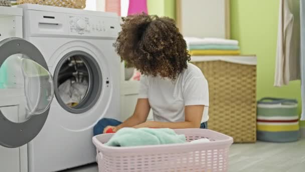 Молода красива іспаномовна жінка миє одяг, сидячи на підлозі, втомившись у пральні - Кадри, відео