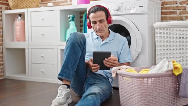 Чоловік середнього віку слухає музику, яка чекає на пральну машинку в пральні - Кадри, відео
