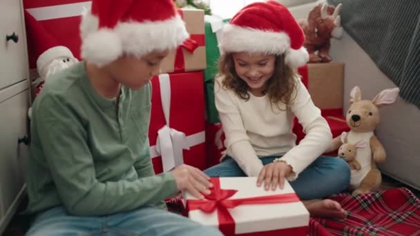 Очаровательный мальчик и девочка распаковывают рождественский подарок с удивительным выражением лица дома - Кадры, видео