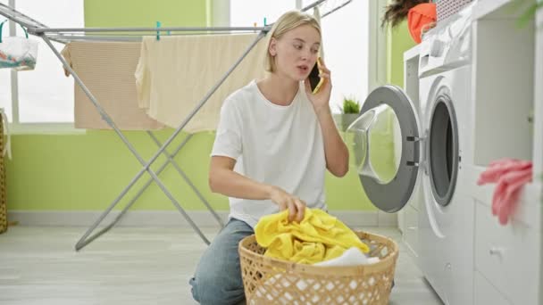 Молода блондинка миє одяг, розмовляючи на смартфоні, злиться в пральні - Кадри, відео