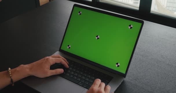 Közelkép férfi szabadúszó dolgozik laptop számítógép zöld képernyős modell, ül az irodában. A vállon lövés üzlet férfi ül az asztalnál, dolgozik a számítógép zöld képernyő chroma - Felvétel, videó