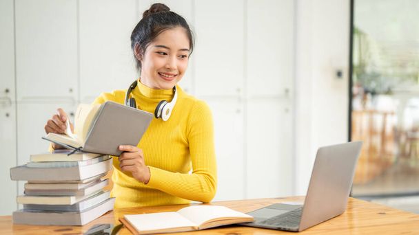 Eine schöne junge asiatische Studentin sucht Informationen in einem Buch, arbeitet an ihrem Schulprojekt, bereitet sich auf eine Prüfung vor und erledigt ihre Hausaufgaben in einer Bibliothek. Bildungskonzept - Foto, Bild